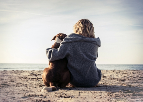 Vrouw zit naast hond op het strand