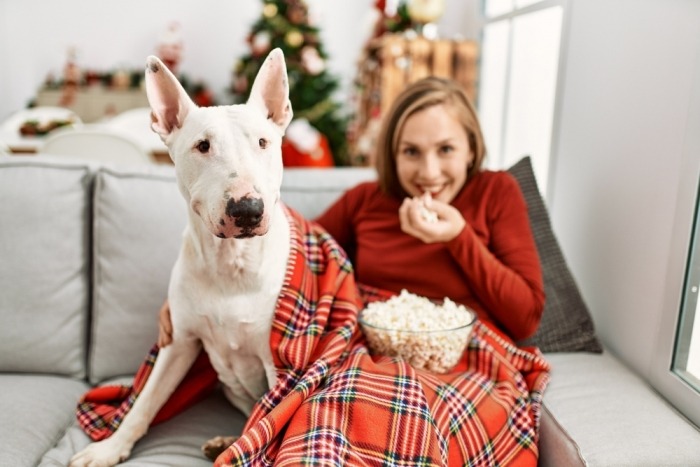Vrouw kijkt film met hond en eet popcorn in de zetel