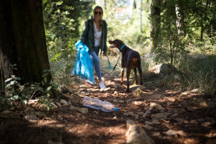 Jonge vrouw ruimt afval op in bos met doberman