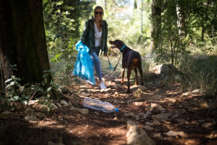 Afval verzamelen hond Jonge vrouw ruimt afval op in bos met doberman