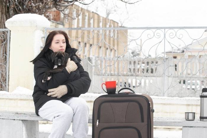 Vrouw met hondje en valies zit buiten te wachten